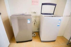 Two stacked washing machines in a corner with a tiled floor and a door with a sign. - Homeinn Pebble Hotel (Qingdao North Station Licun Pedestrian Street) (Qingdao)