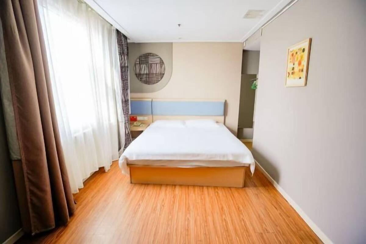 A hotel room with a bed, wooden flooring, a headboard, a wall-mounted circular artwork, and a framed picture.