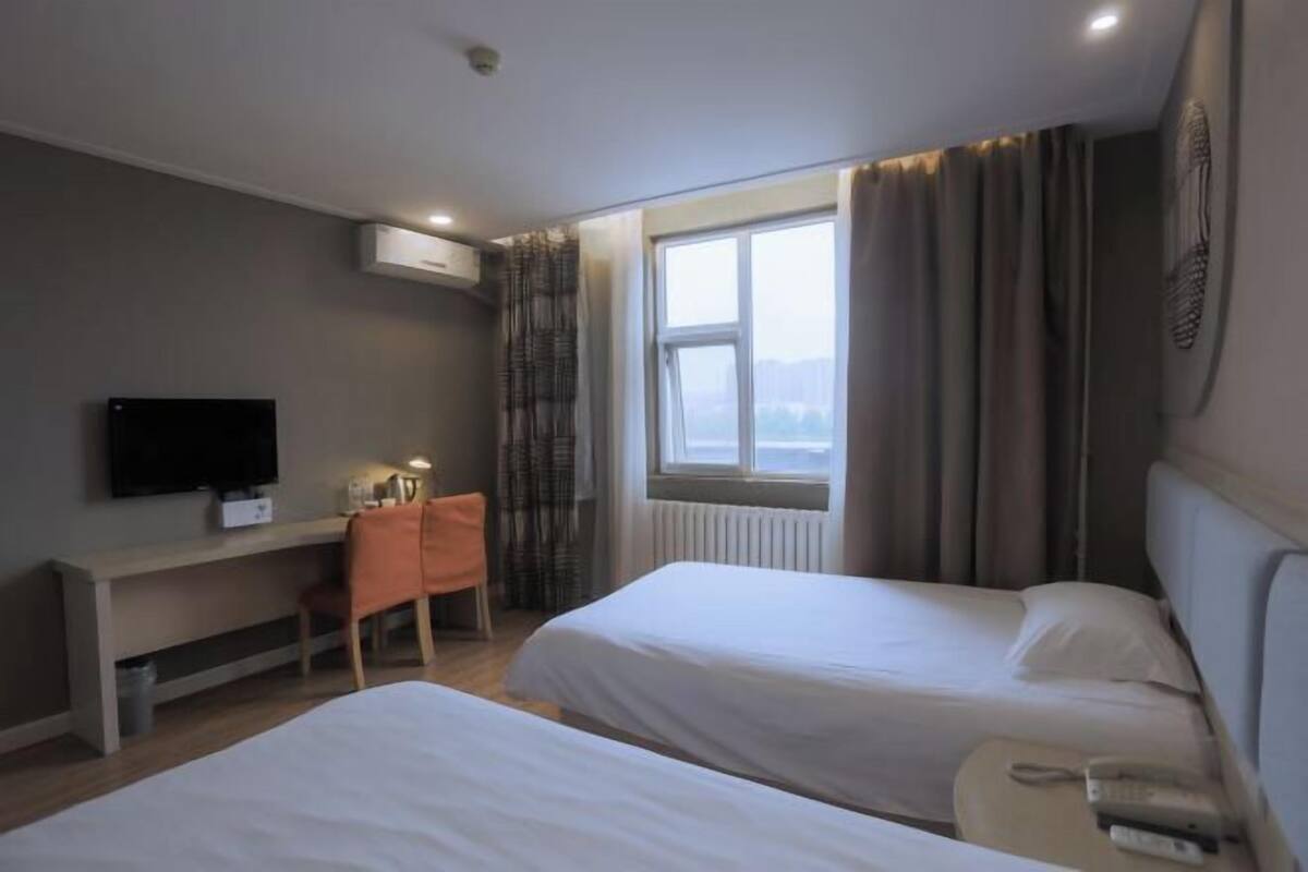 A hotel room with two beds, a desk with a chair, a television, and a window with curtains.