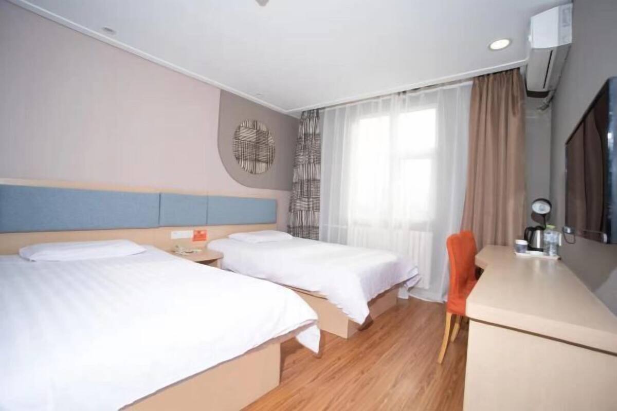 A hotel room with two beds, a desk, a chair, a mirror, and a window with curtains.