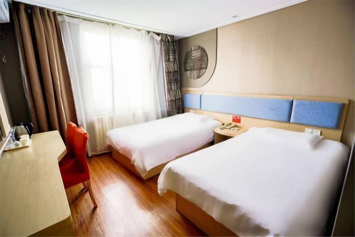 A hotel room with two beds, a desk, a chair, a round wall decoration, and a window with curtains.
