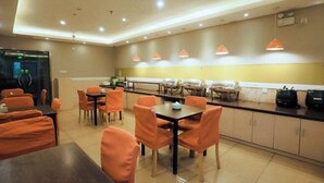 A modern dining area with orange chairs and tables, a kitchen counter with appliances, and pendant lighting. - Homeinn Pebble Hotel (Qingdao North Station Licun Pedestrian Street) (Qingdao)