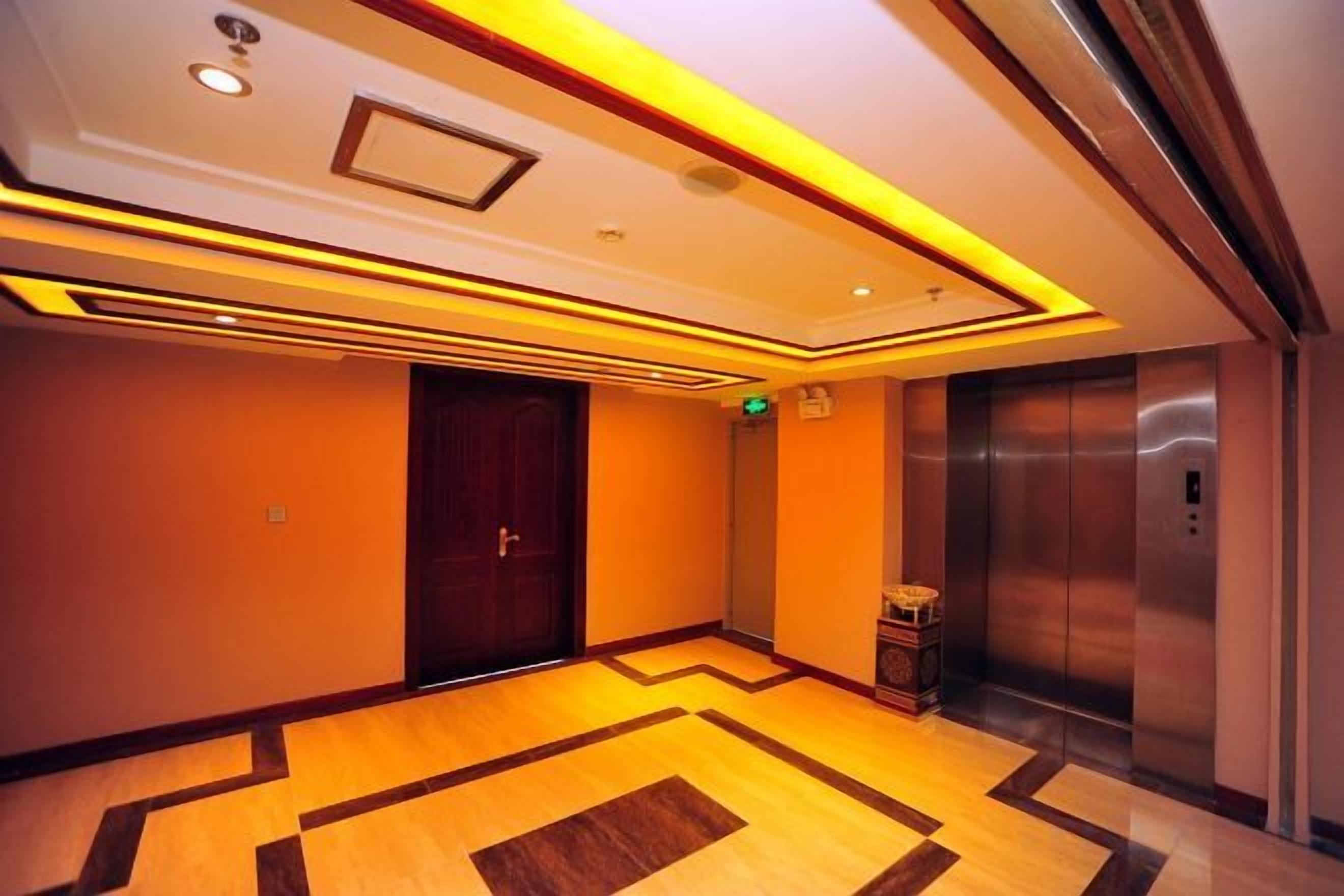 A hotel lobby with a wooden floor, a door, an elevator, and a wall-mounted light fixture.