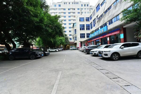 Un parking avec plusieurs voitures, un bâtiment avec des panneaux indicateurs et un arbre.
