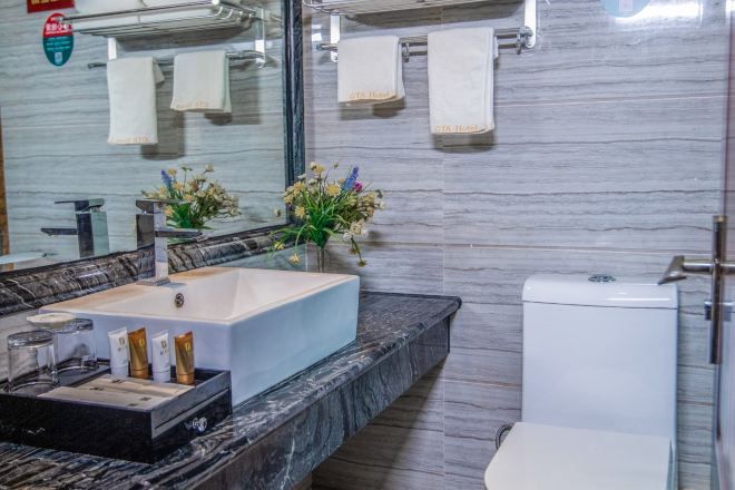 Ein Badezimmer mit Marmorplatte, Waschbecken, Toilette und Handtüchern an einem Haken.