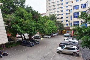 Een parkeerplaats met meerdere auto's, bomen en een gebouw met meerdere verdiepingen op de achtergrond.