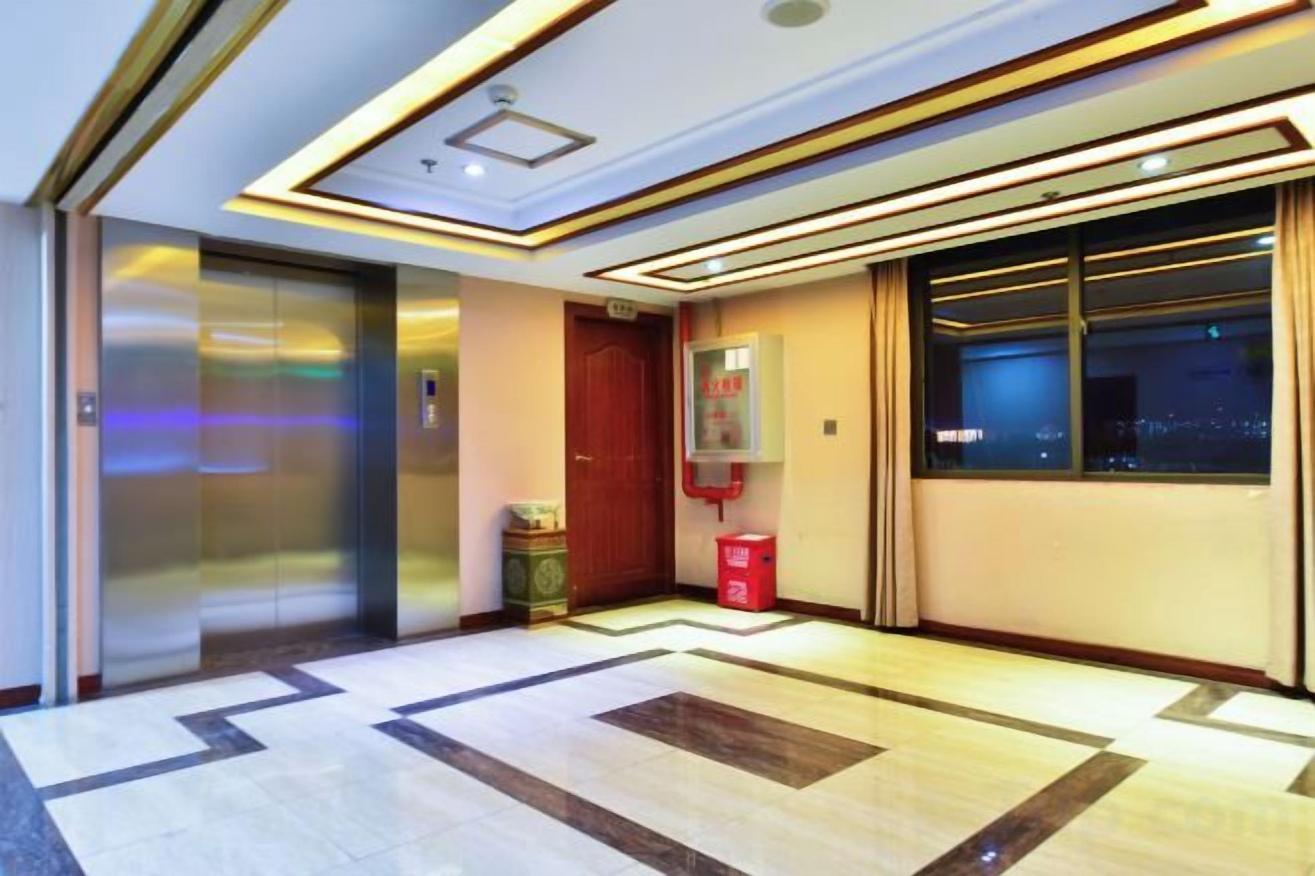 A hotel lobby with a modern design, including a reception desk, a red door, and a large window offering a city view.