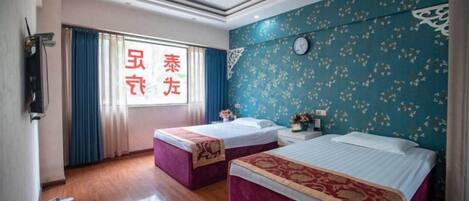 A hotel room with two beds, a large window with curtains, a clock on the wall, and a patterned wallpaper.