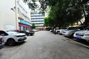 A parking lot with multiple cars, a building with signage, and trees. - Gemeng Hotel (Xishuangbanna Xuanwei Avenue) (Jinghong)