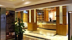 A hotel reception area with a modern design, featuring a reception desk, decorative panels, and a large potted plant. - Gemeng Hotel (Xishuangbanna Xuanwei Avenue) (Jinghong)