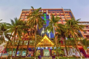 A multi-story hotel with a central atrium, palm trees, and a prominent entrance with a decorative arch. - Gemeng Hotel (Xishuangbanna Xuanwei Avenue) (Jinghong)