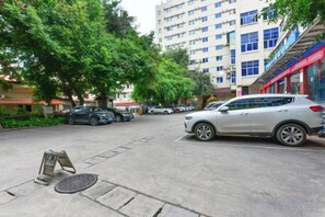 A street with parked cars, trees, and a building with multiple floors and windows. - Gemeng Hotel (Xishuangbanna Xuanwei Avenue) (Jinghong)