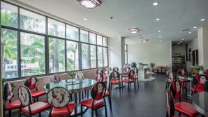A dining area with round tables and chairs, large windows with a view of palm trees, and a modern interior design. - Gemeng Hotel (Xishuangbanna Xuanwei Avenue) (Jinghong)