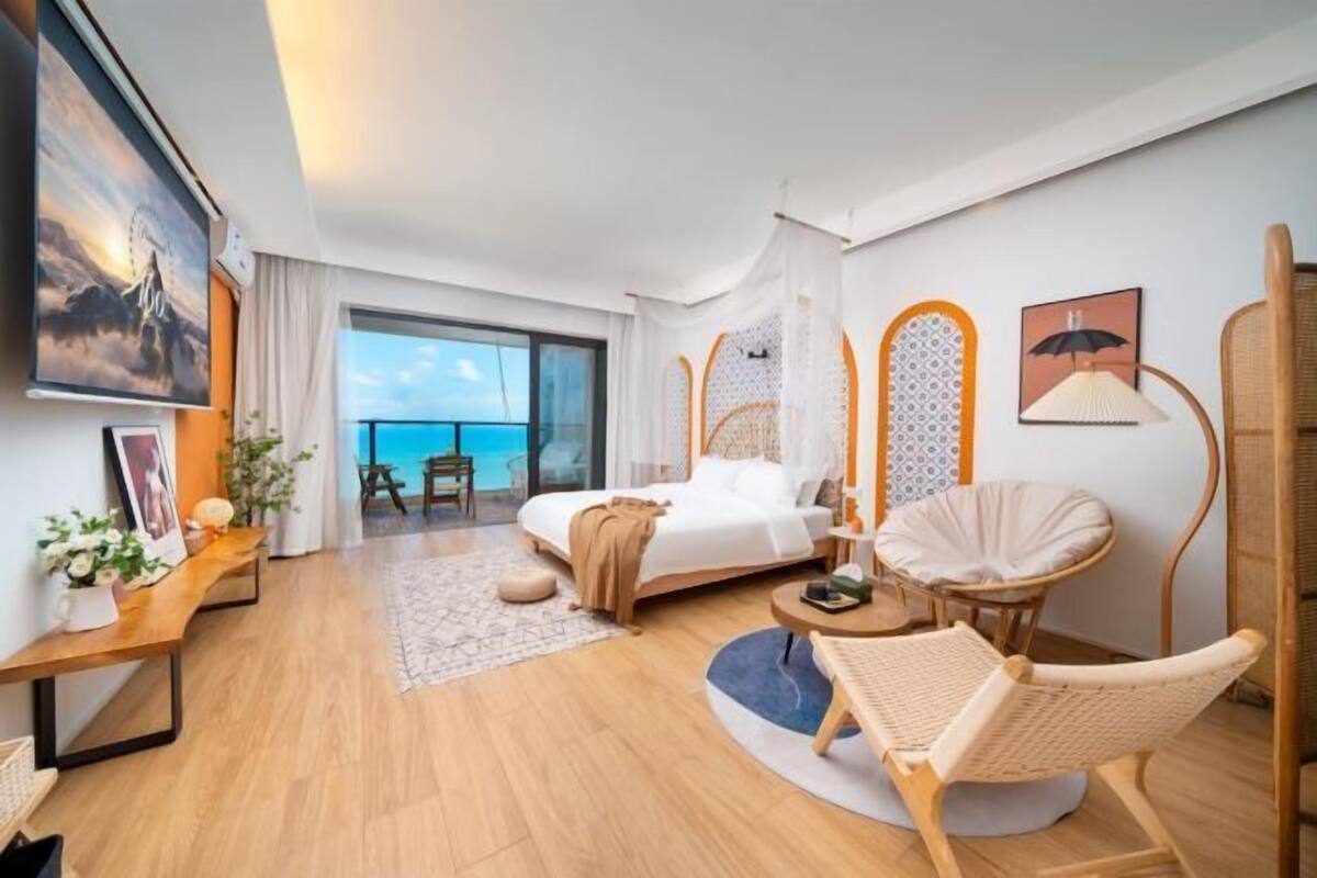 Een hotelkamer met een bed, een stoel, een tafeltje, uitzicht op zee en een balkon.