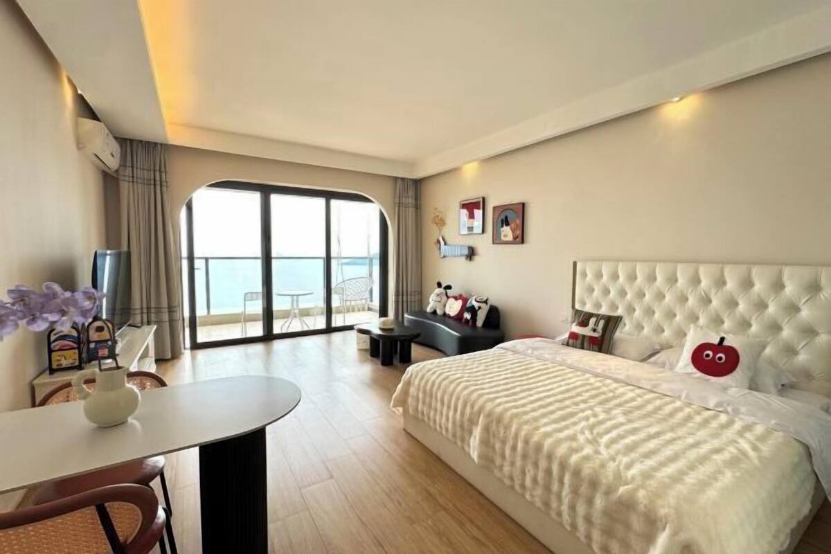 Een moderne hotelkamer met een groot bed, een eettafel en uitzicht op zee door een groot raam.