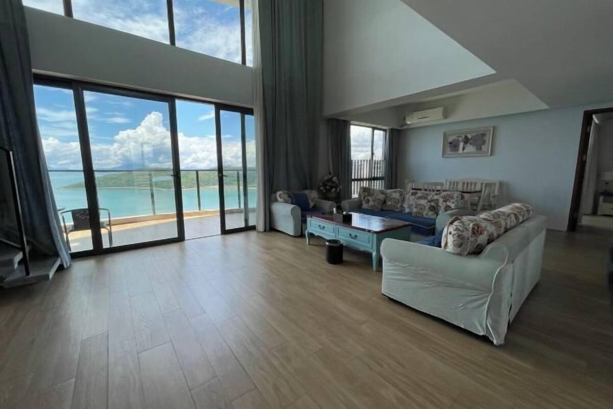 Een ruime woonkamer met een grote schuifpui die uitkomt op een balkon met uitzicht op het water.