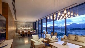 Une chambre d’hôtel moderne dotée d’une grande fenêtre, d’un coin repas et d’un espace salon avec des canapés et une table basse.