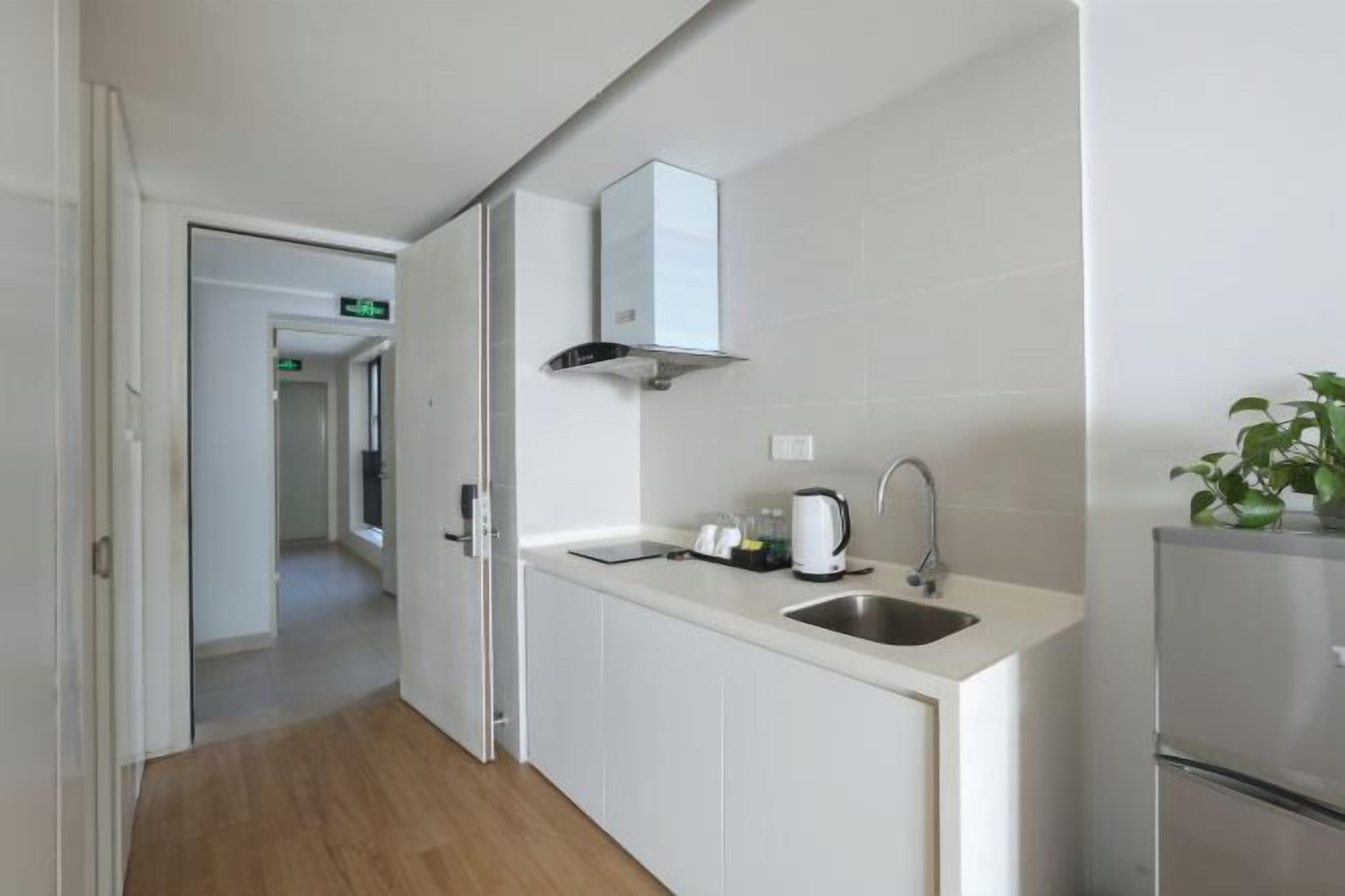 A modern kitchen with white cabinets, a stainless steel sink, a built-in range hood, and a refrigerator.