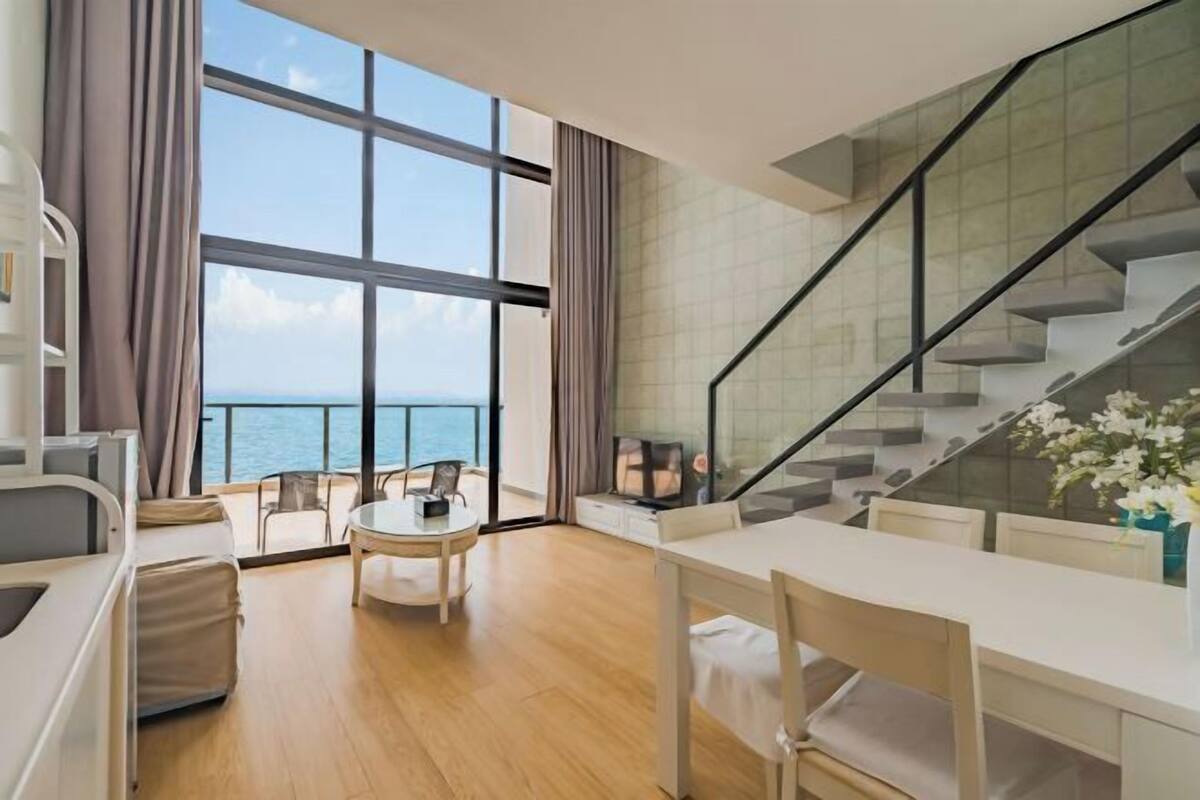 Een moderne hotelkamer met een groot raam, een zithoek en een trap.