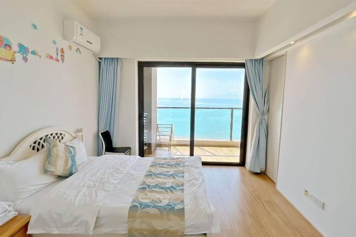 Een slaapkamer met een bed, een stoel, een balkon met uitzicht op zee en een airconditioning.