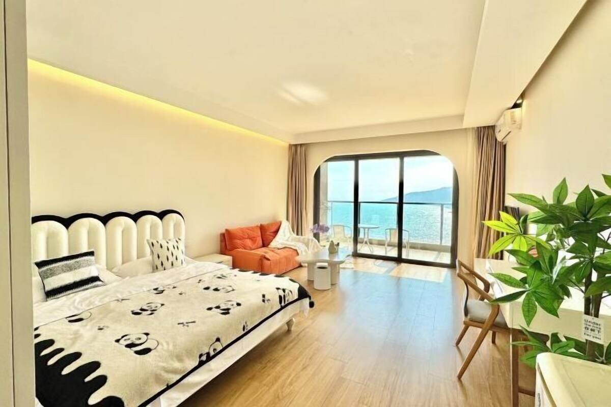 Een hotelkamer met een bed, een bank, een klein tafeltje, een stoel en een groot raam met uitzicht op de zee.
