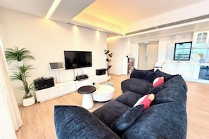 A modern living room with a large grey sofa, a flat-screen TV, and a white console table.