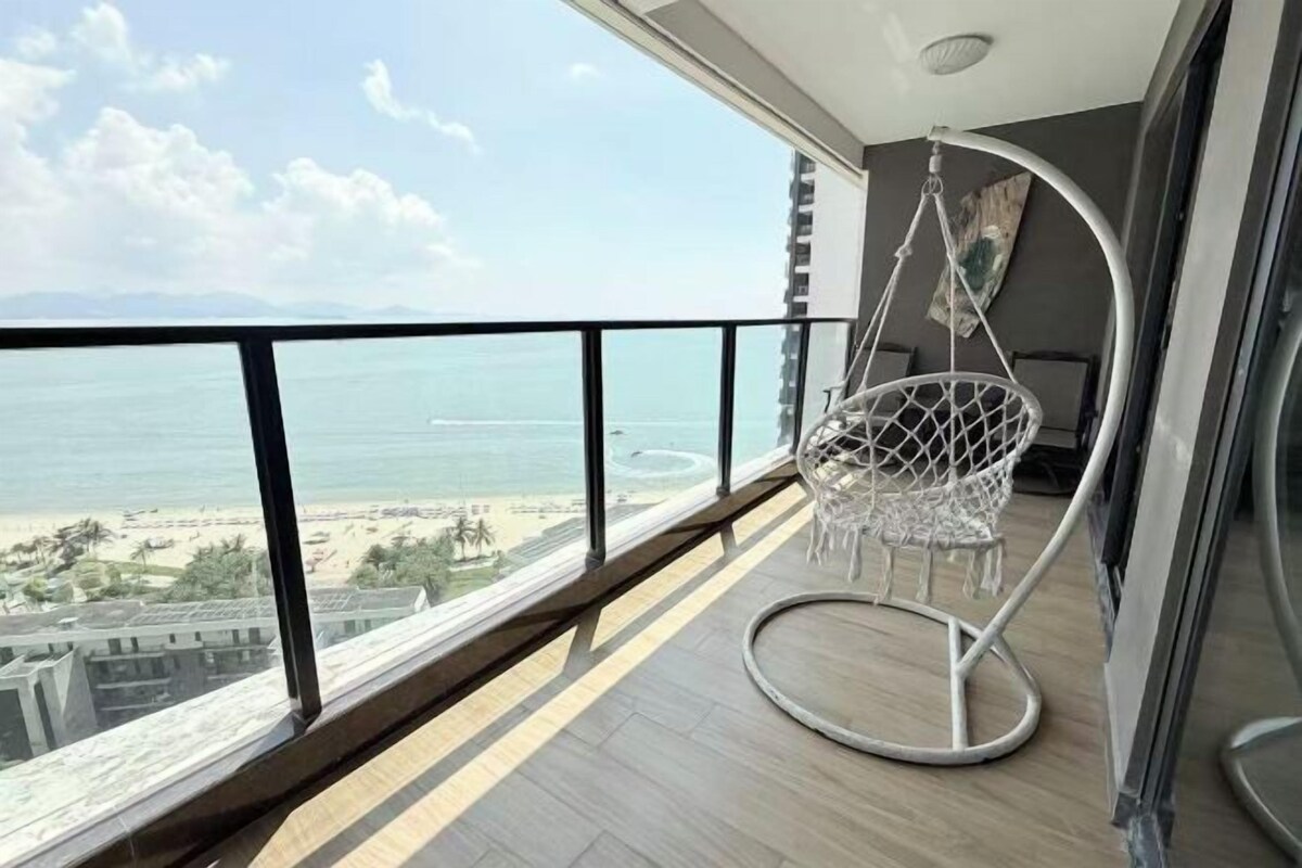 Un balcon avec un fauteuil suspendu, une vue sur la mer et un bâtiment en arrière-plan.