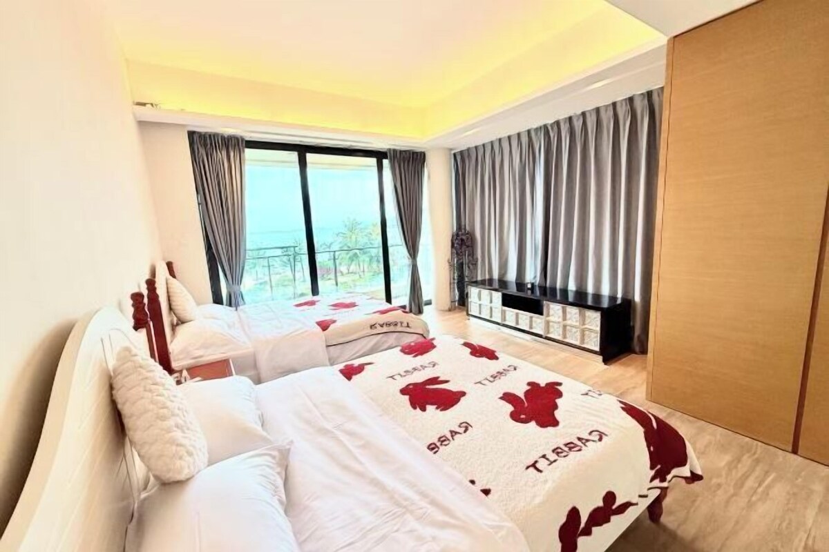 A bedroom with two beds, a large window with curtains, a TV stand, and a wardrobe.