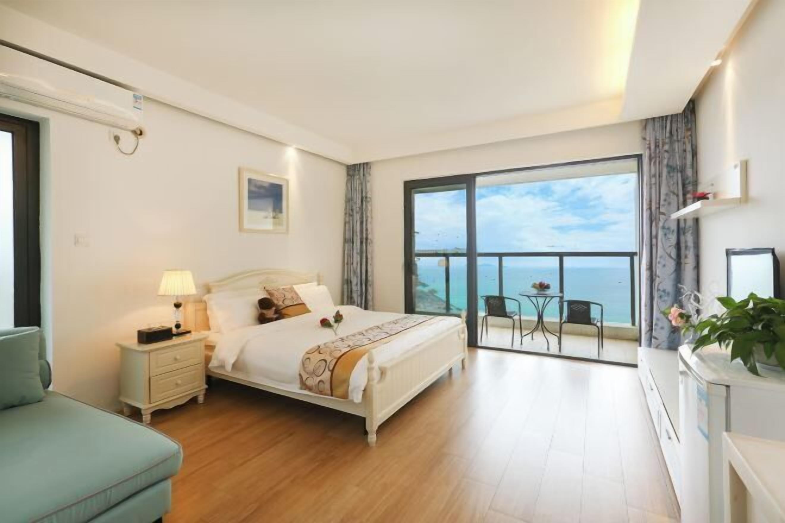 A bedroom with a large bed, a nightstand, a chair, and a view of the ocean through a balcony.