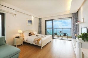 A bedroom with a large bed, a nightstand, a chair, and a view of the ocean through a balcony. - Relais Boutique Apartment (Huizhou Huarun Xiaojingwan) (Huizhou)