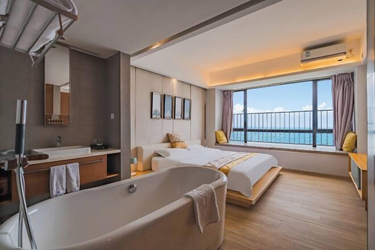 Een moderne hotelkamer met een ruime badkuip, een balkon met uitzicht, een tweepersoonsbed en een groot raam.