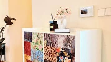 Ein Empfangsschalter mit einer floralen Stegdecke, einer Blumenvase, einem kleinen Radio und einem Thermostat an der Wand.