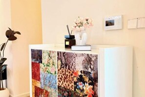 A reception desk with a floral quilt, a vase with flowers, a small radio, and a thermostat on the wall. - Relais Boutique Apartment (Huizhou Huarun Xiaojingwan) (Huizhou)