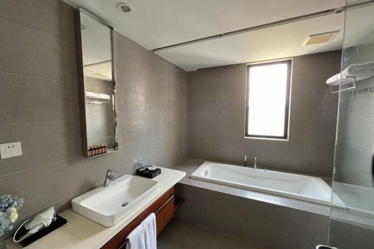 A modern bathroom with a large mirror, a sink, a bathtub, and a window providing natural light.
