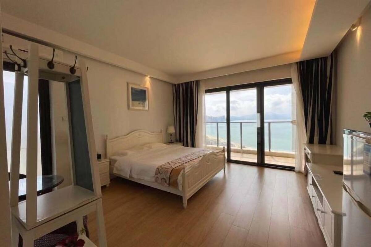 Een hotelkamer met een bed, een kledingkast, een bureau en een groot raam met uitzicht op zee.
