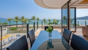 Un balcon avec une table et des chaises en verre, donnant sur une plage bordée de palmiers et sur la mer.