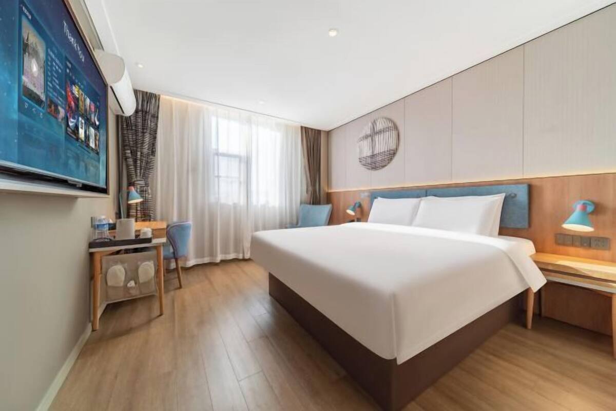 Une chambre d’hôtel avec un grand lit, un bureau avec une chaise, un téléviseur fixé au mur et une fenêtre avec des rideaux.