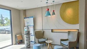 A modern reception area with two leather armchairs, a small round table, and a blue ottoman. There is a poster on a pillar and a large wall-mounted light fixture. - HomeInn·neo（Linyi Hedong District government store） (Linyi)