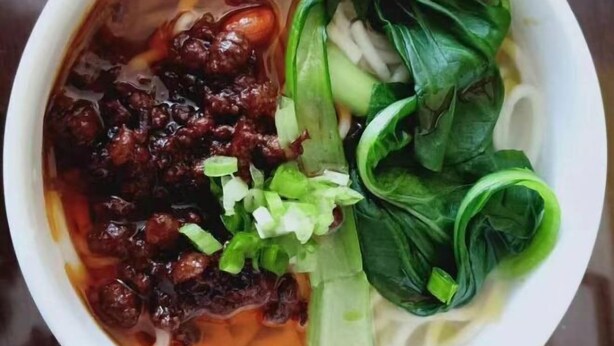 Un bol de sopa amb fideus, verdures i una salsa fosca.