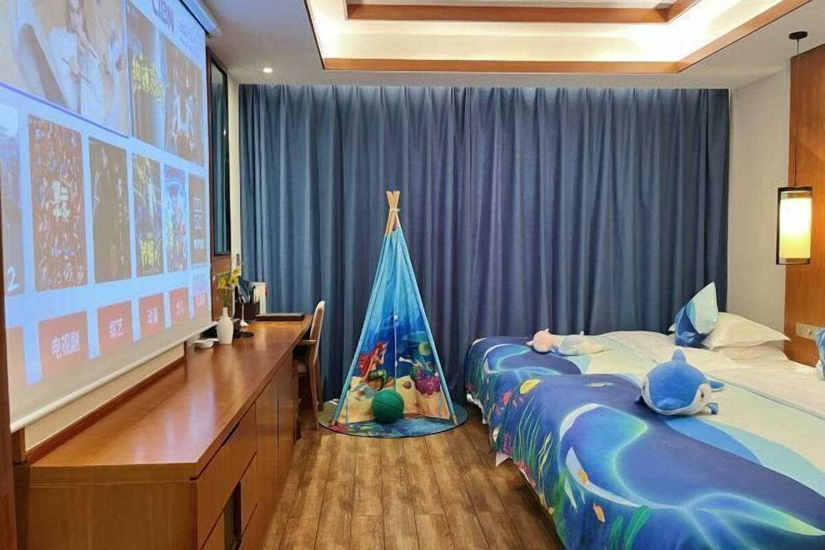 A hotel room with a bed, a desk, a projector screen, and a tent-like play area.