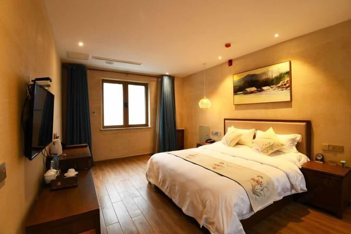 A hotel room with a large bed, a television, a painting on the wall, and a window with curtains.