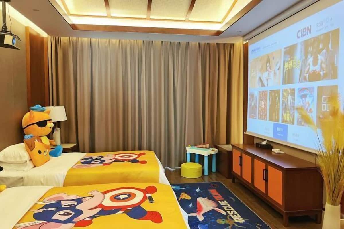 A hotel room with two beds, a television, a small table, and a projector screen displaying images.