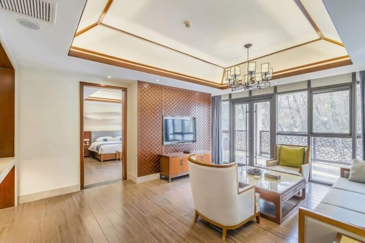 A modern hotel room with a wooden floor, a sofa, a TV, and a large window.