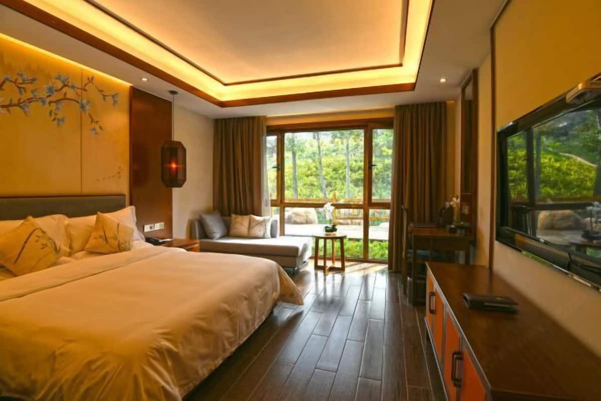 A hotel room with a large bed, a seating area with a view, and a TV.
