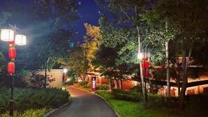 A pathway leading to a building with traditional architecture, surrounded by greenery and illuminated by red lanterns.