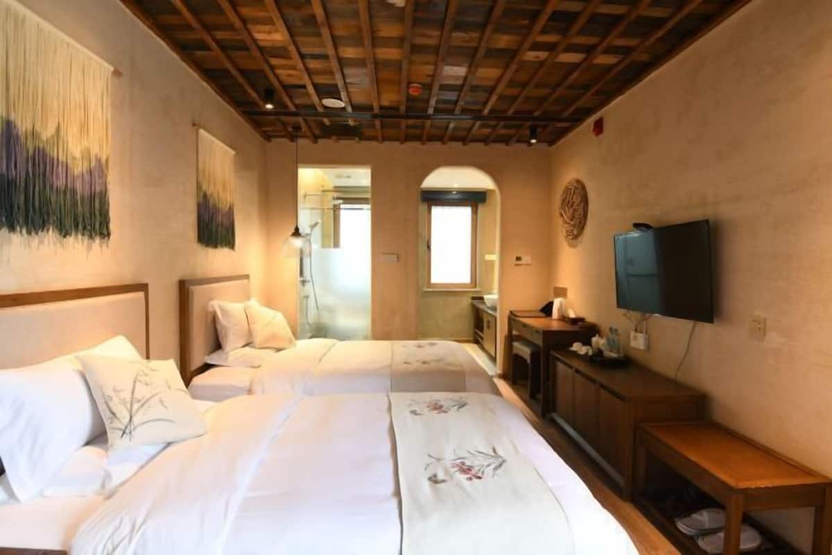 A hotel room with two beds, a TV, a wooden cabinet, and a mirror.