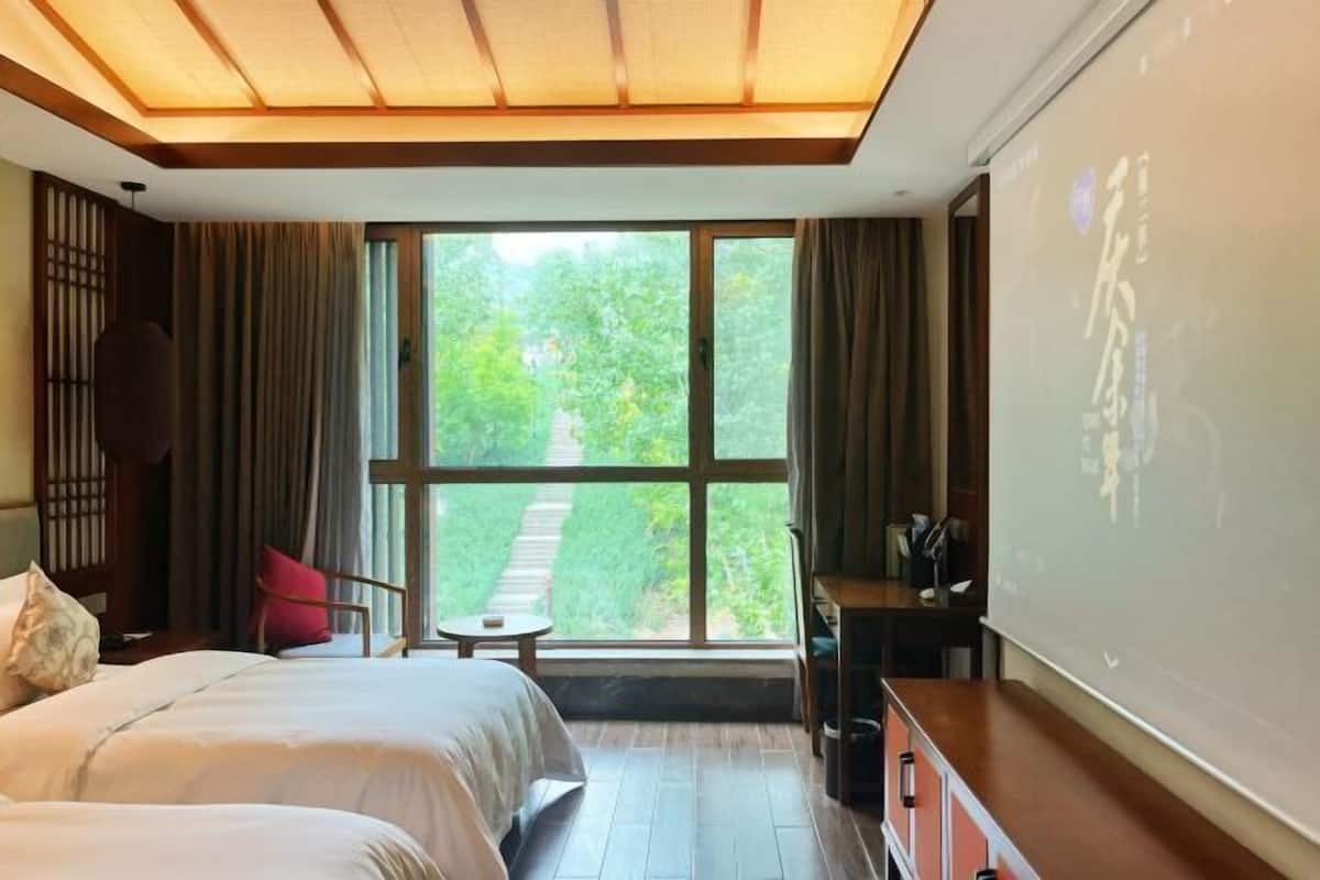 A hotel room with a large window, a bed, a desk, and a projector screen.
