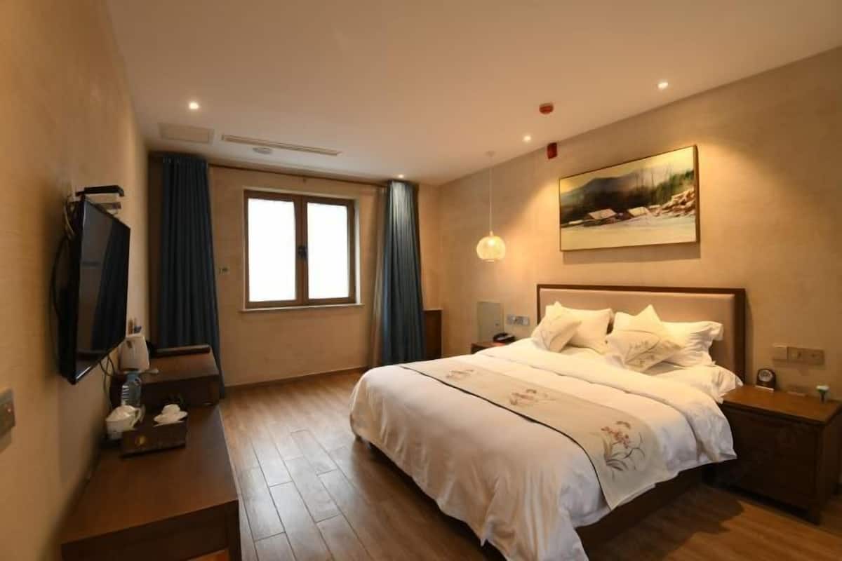 A hotel room with a large bed, a flat-screen TV, a painting on the wall, and a window with curtains.