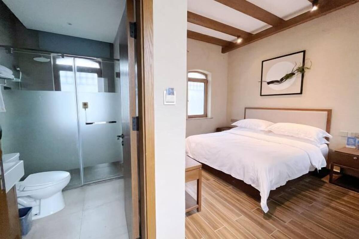 A room with a bed, a bedside table, a window, and a door leading to a bathroom.