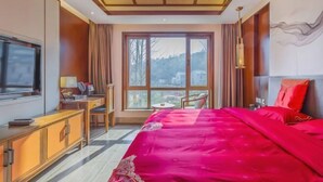 A hotel room with a large bed, a desk with a chair, a television, and a view of the outdoors through a large window.